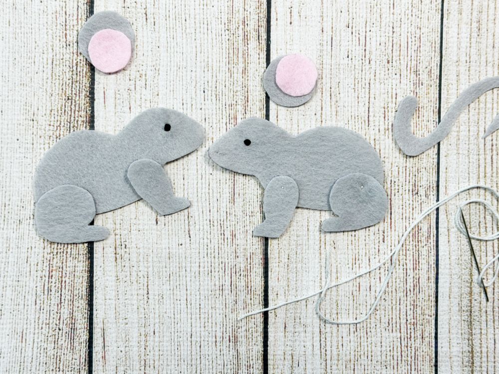 Hand sewing black eyes onto a felt mouse plushie with embroidery floss.
