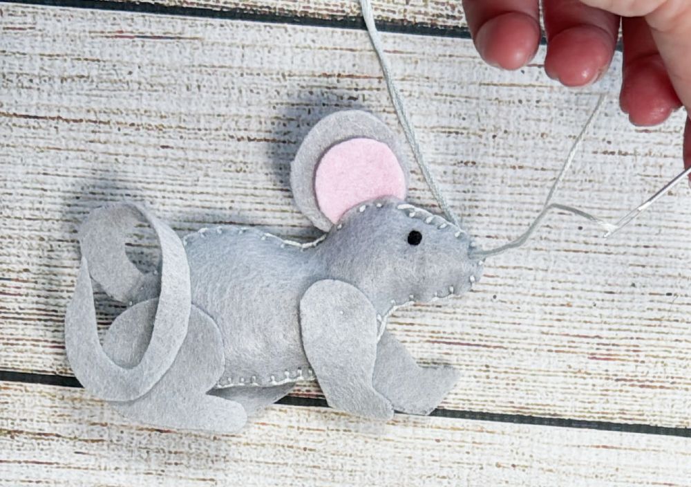 Adding black whiskers with thread to a grey felt mouse plushie.