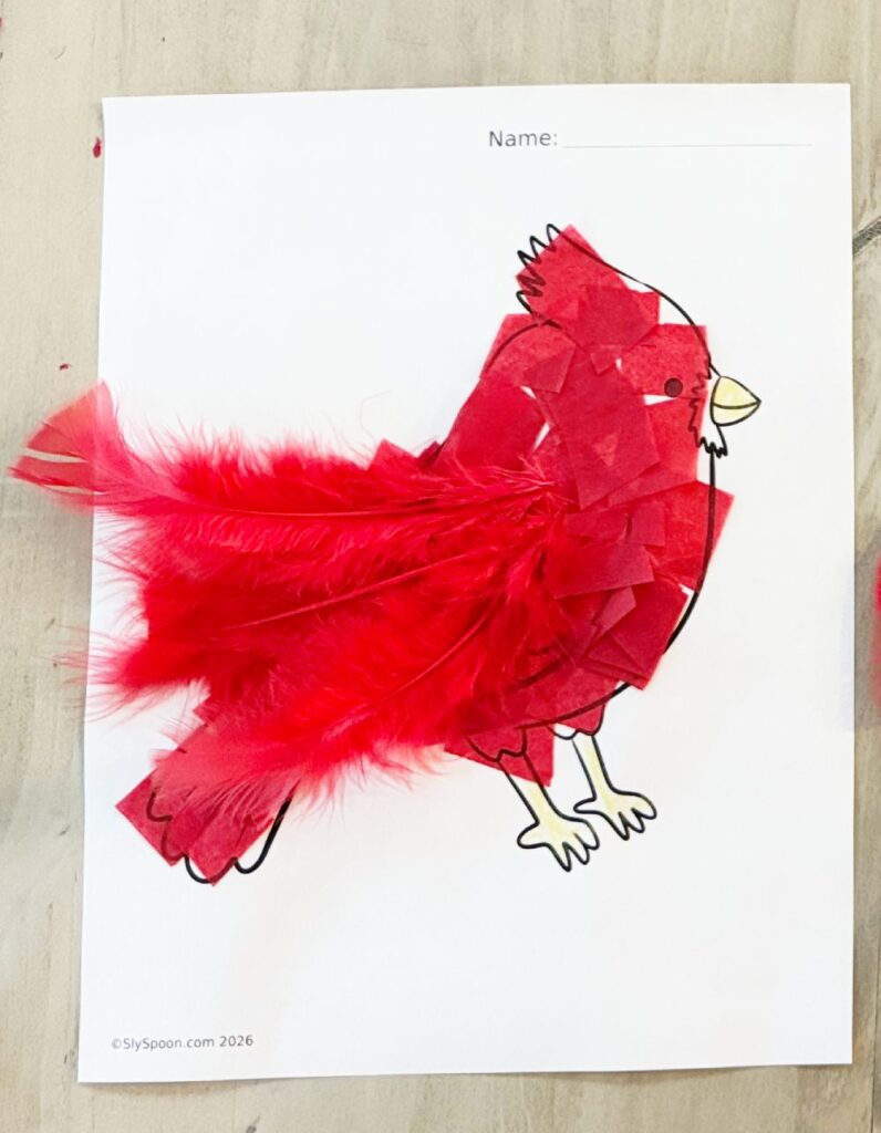 Winter cardinal craft where the bird’s body is filled in with crumpled red tissue paper and red feathers added for wings.