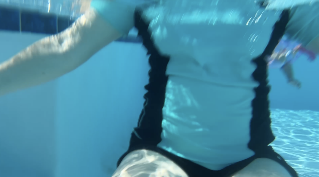 Mom wearing a Halcurt built-in bra rash guard while supervising children at a neighborhood swimming pool.