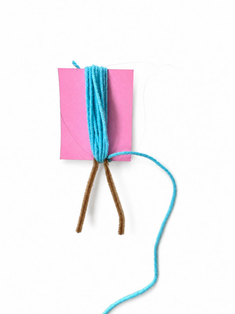 Yarn wrapped around a 3 inch measuring card with a pipe cleaner attached to make hair for a DIY mermaid doll.